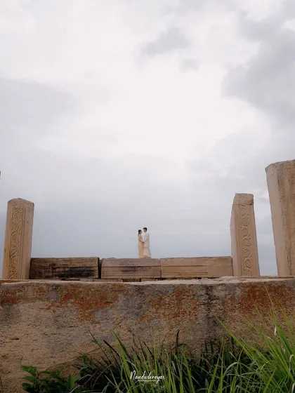 An architectural shot of a couple embracing atop a large stone structure, emphasizing the grandeur of the location.