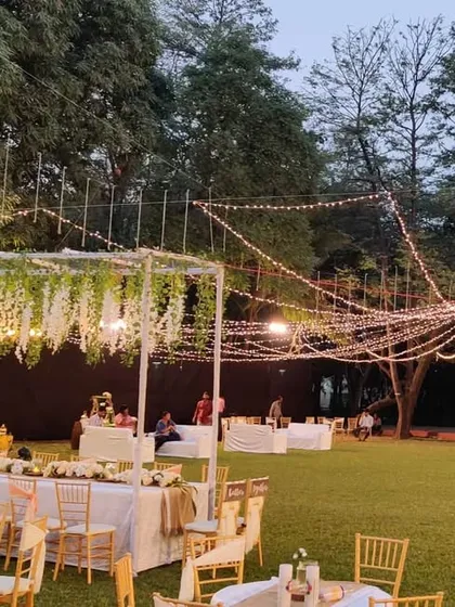A wider view of the rustic reception setup, showing the head table, guest seating area, and the beautiful string light canopy. We designed the layout to make the large lawn feel cozy and connected.