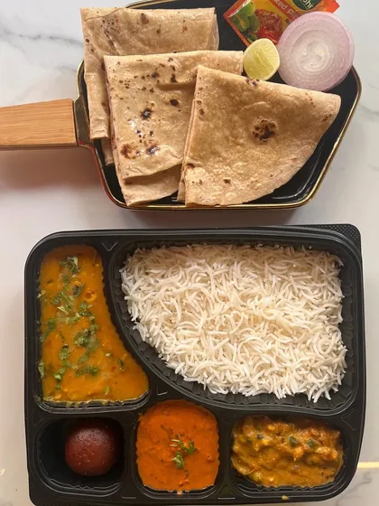 Another view of our popular North Indian thali meal box. This overhead shot clearly displays the different components: dal tadka, paneer sabzi, a dry vegetable dish, rice, rotis, and a sweet, all ready to be enjoyed.