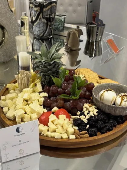 A close-up of a bespoke charcuterie platter created for the luxury decor brand, Maison Sia. This board highlights a rich assortment of artisanal cheeses, plump grapes, dried fruits, and nuts, with fresh pineapple and bocconcini balls adding a unique touch.
