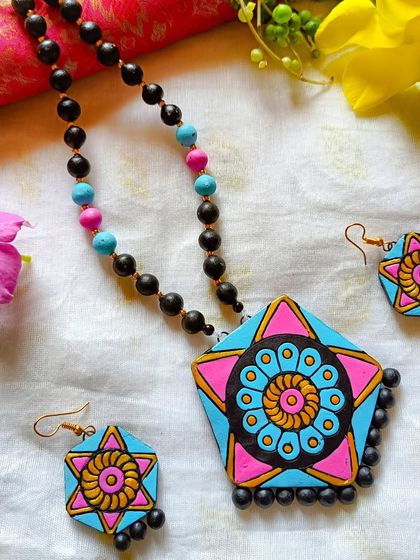 This necklace features a hexagonal pendant with a mandala-style flower painted in the center. The combination of pink, blue, and yellow is bright and cheerful.