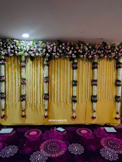 A simple and elegant backdrop with thick, hanging garlands of jasmine and roses. The golden curtain provides a rich and warm background for any traditional ceremony.
