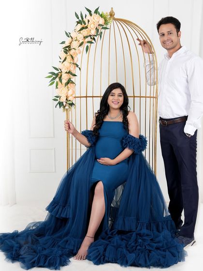 A stylish couple portrait featuring a deep blue gown and a golden birdcage prop. The elegant setup and their happy expressions make for a beautiful memory.