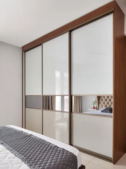 A full-height, floor-to-ceiling sliding wardrobe with Aristo doors. The design combines back-painted glass with a central tinted mirror panel, which reflects the bedroom and makes the space feel larger and brighter.
