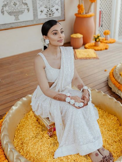 A beautiful Haldi look in all-white. The bride wears a stunning white saree with floral jewelry, paired with a 'no-makeup' makeup look and a traditional gajra braid for a serene and elegant vibe.
