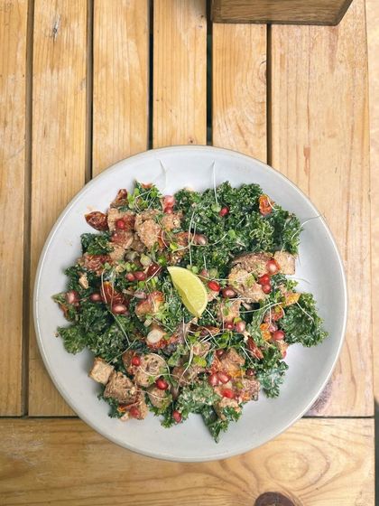 Another view of our vibrant kale salad, showcasing the fresh greens and colourful pomegranate seeds on a rustic wooden table. Healthy eating can and should be beautiful.
