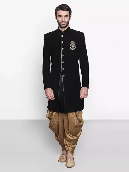 A classic black sherwani jacket with an embroidered crest, paired with a golden dhoti. This look is bound to make heads turn at any wedding.