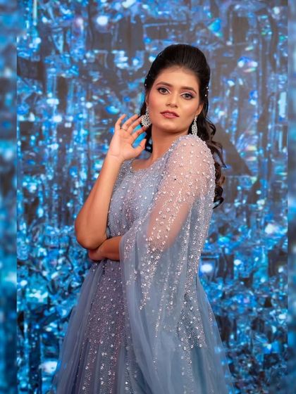 A striking portrait against a sparkling blue background. This gown with its delicate cape sleeves is perfect for a glamorous party look.