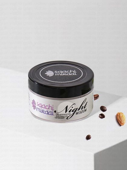 A clean, angled shot of Saachi Mirai's Night Wisdom cream on a white block, with key ingredients like almonds and coffee beans nearby. This is a classic product styling technique for e-commerce.