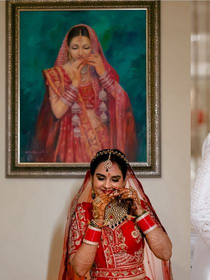 A candid moment of the bride adjusting her necklace, captured as she stands before a painting, creating a beautiful blend of art and life.