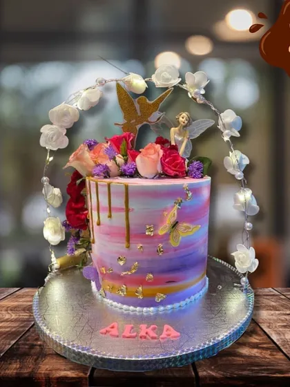 A fairy-themed cake that looks like it came from an enchanted garden. It features a beautiful watercolor buttercream finish, gold drips, and is topped with fresh flowers, a fairy, and butterflies.