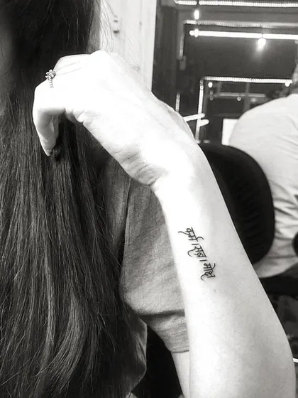 A black and white shot of a delicate 'Ant asti prarambh' script tattoo on the wrist, showcasing its elegant placement.