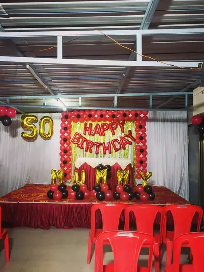 A classic red and black stage decoration for a 50th birthday party. The setup includes a balloon frame, 'MUMMY' foil letters, and seating arrangements for guests.