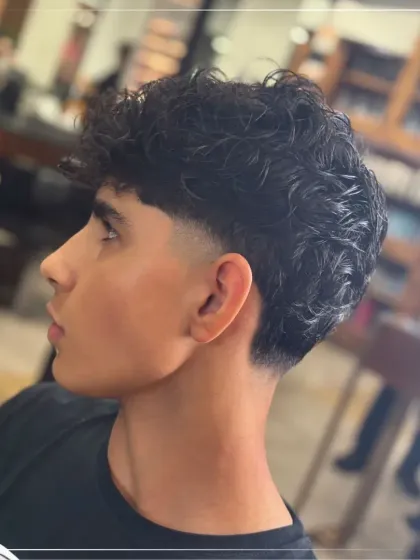 For our clients with curly hair, we specialize in cuts that enhance natural texture. This style combines a neat fade with well-defined curls on top, creating a look that is both stylish and manageable.