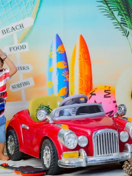 This little one is ready to cruise down the boardwalk in his red toy car, part of our fun and versatile beach theme.