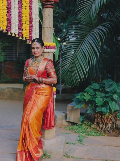 A stunning solo portrait of the bride in her vibrant orange and red Kanjeevaram saree, a classic look for a South Indian bride.