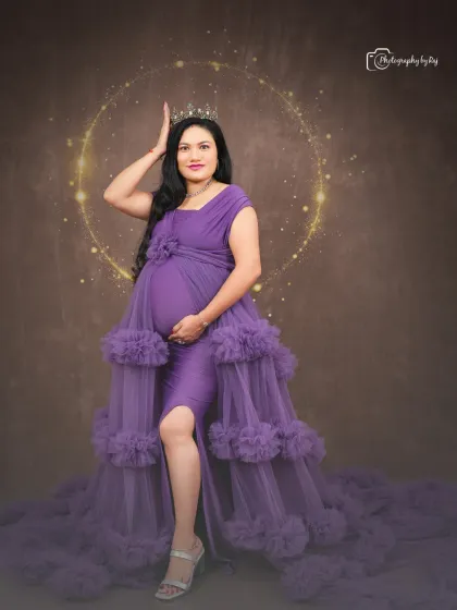 A glamorous studio portrait of a mother-to-be in a purple ruffled gown and crown.