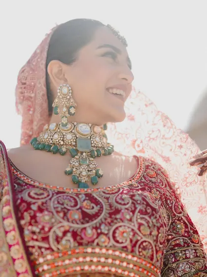The pure, uninhibited joy of a bride on her wedding day. This candid close-up captures a genuine smile, highlighted by the sun and the sparkle of her stunning polki and emerald jewelry, a key part of her styled look.