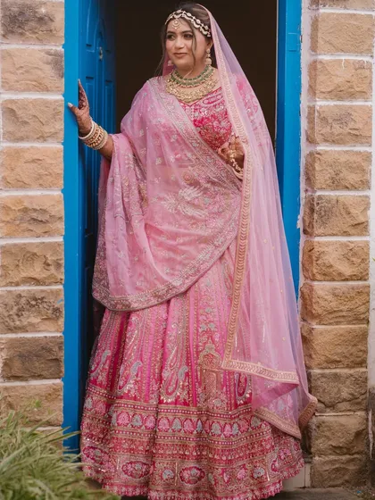 A beautiful bride framed by a vibrant blue doorway. The contrast of colors makes her pink lehenga pop, creating a striking and memorable bridal portrait.