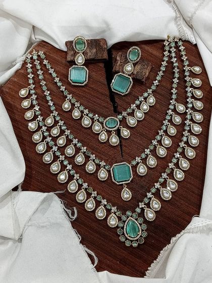 A grand, three-layered AD necklace set. This piece is designed for maximum impact, featuring square and teardrop stones, and is available in blue, green, pink, and red.