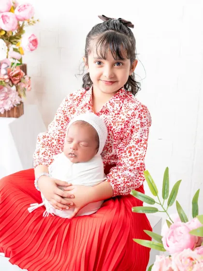A proud big sister holds her newborn sibling for the first time. This heartwarming shot captures the beginning of a lifelong bond, set against a soft floral background.