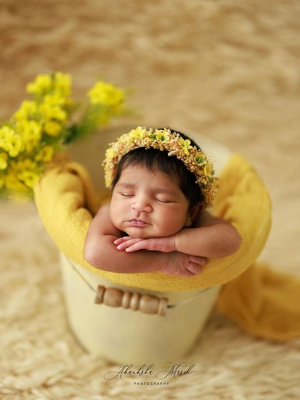 A little ray of sunshine. This newborn is posed in a bucket with warm, yellow tones and matching floral accents, creating a bright and cheerful portrait that feels full of warmth.