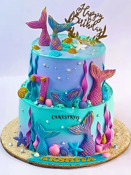 A beautiful two-tier mermaid cake combining chocolate and vanilla flavors. The aqua and lavender design is decorated with fondant mermaid tails, starfish, and seashells for a 7th birthday.