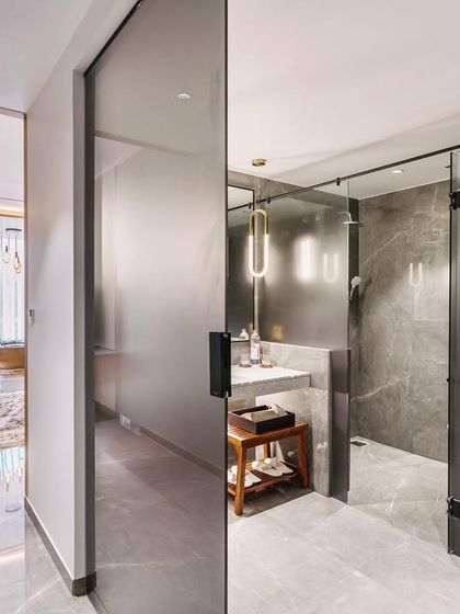 The bathroom design continues the theme of quiet luxury with sleek, modern fixtures and materials. A frosted glass sliding door provides privacy while allowing light to pass through, connecting it to the main room and enhancing the sense of space.