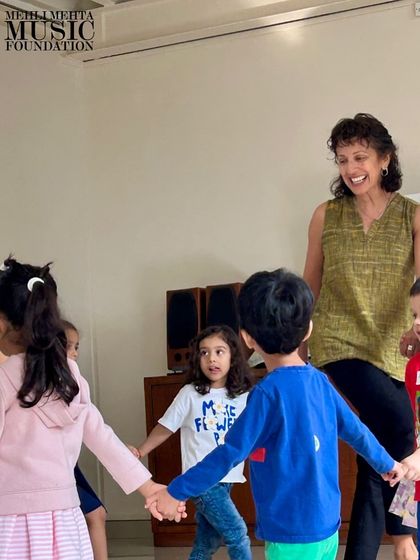 Children hold hands and move in a circle with their teacher. Group activities like this teach cooperation, listening, and the joy of making music together.