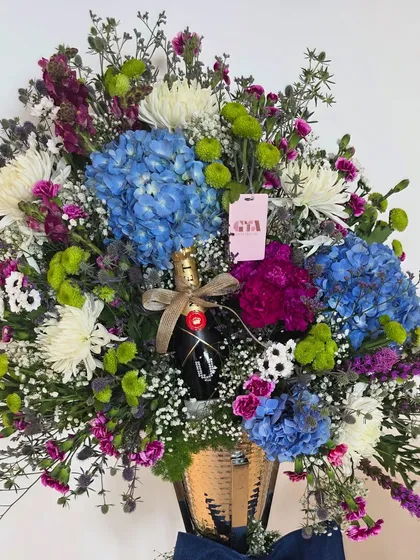 A close-up of a vibrant, celebratory hamper. I paired a bottle of premium champagne with a lush arrangement of blue hydrangeas, chrysanthemums, and purple statice, all set in a textured gold vase for a touch of glamour.