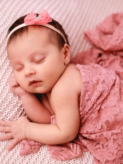 A delicate lace wrap in soft pink adds a touch of elegance. Posed on a textured blanket, this classic shot focuses on the baby's serene expression.