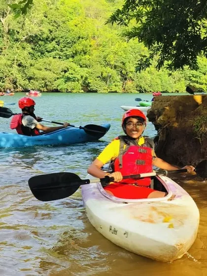 Two young kayakers paddle near the shore, gaining confidence in a safe and supervised area.