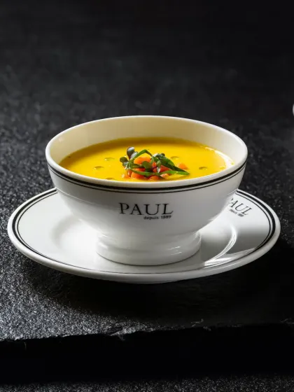 A warm bowl of lentil soup from Paul, garnished with fresh herbs, shot with dramatic lighting against a dark background.