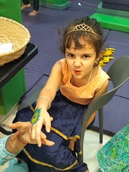 A little girl getting a peacock feather painted on her hand for a Janmashtami celebration. Our talented artists can create designs for any theme or occasion.