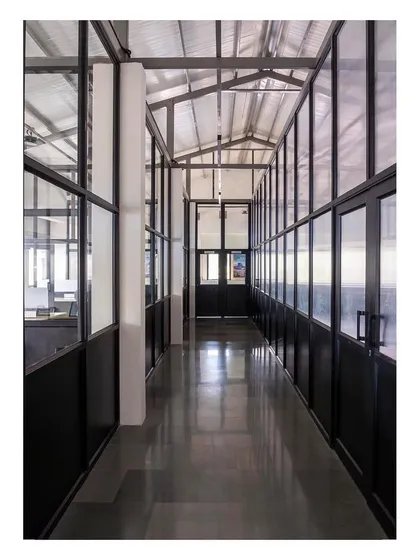 The main interior corridor of the office space. The use of glass partitions and a lofty roof with skylights allows natural light to flood the area, creating a spacious and visually connected working environment.