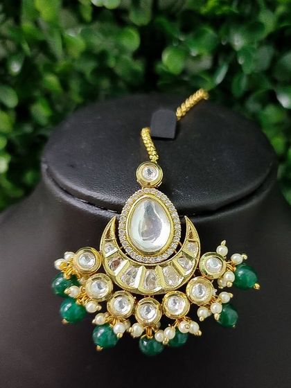 A lovely chaand bali style maang tikka with a large central kundan stone and green bead drops.