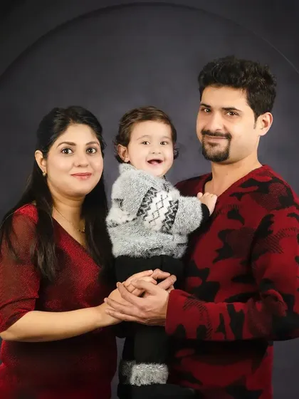 A warm family portrait with a smiling baby held between his parents. The coordinated red and grey sweaters are perfect for this cozy, fine-art style.