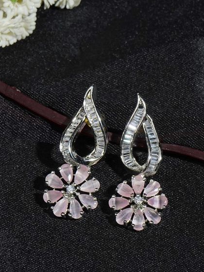 Pink and silver floral earrings on a dark, textured background. The composition draws the eye directly to the product, highlighting its color and design.