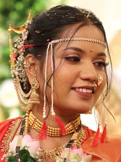 A close-up of a bride in a red Nauvari, her smile lighting up her face. The makeup features a warm, rosy blush and a perfectly matched lip color.