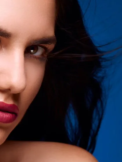A cropped beauty headshot with a focus on the eyes and lips. The hint of hair in motion adds a dynamic element to this otherwise clean and sharp studio portrait against a blue backdrop.