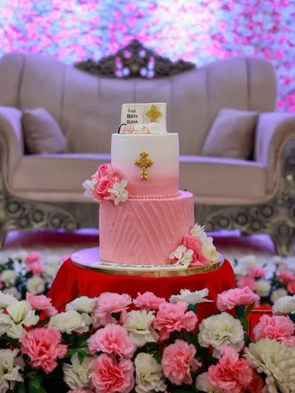Celebrating baby Olivia's baptism with this two-tiered pink cake. The design includes a pink ombre top tier, a textured bottom tier, and is adorned with fresh flowers and gold crosses.
