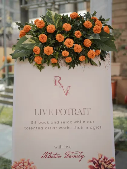 A repeat of the "Live Portrait" sign, topped with a fresh arrangement of marigolds, seamlessly integrating this unique activity into the overall Haldi decor.