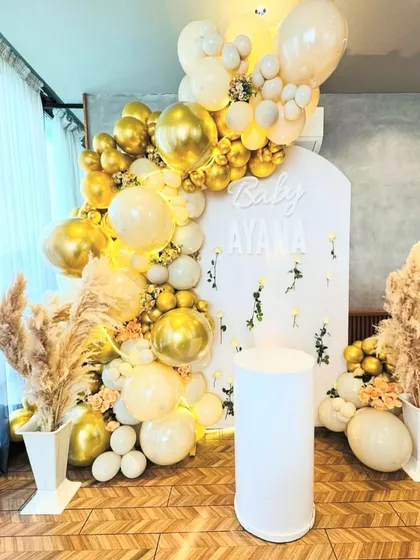 The main photo backdrop for the 'Baby Ayana' Aqeeqa, featuring a cascade of metallic gold and cream balloons, dried pampas, and a custom name sign.