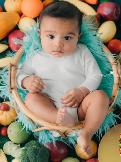 This little one is taking in the colorful world around him. The fruit and veggie setup makes for a vibrant and unique milestone photo.