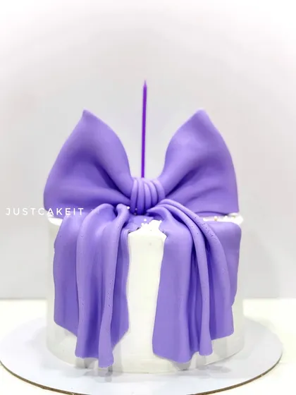 A modern and classy anniversary cake featuring a large, edible purple bow. This trending design is both simple and incredibly elegant.