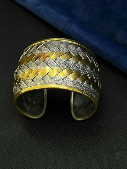 A statement dual-tone cuff with a unique woven pattern. The interplay of matte silver and brushed gold textures gives this piece a modern and sophisticated look. It's a versatile cuff for any occasion.