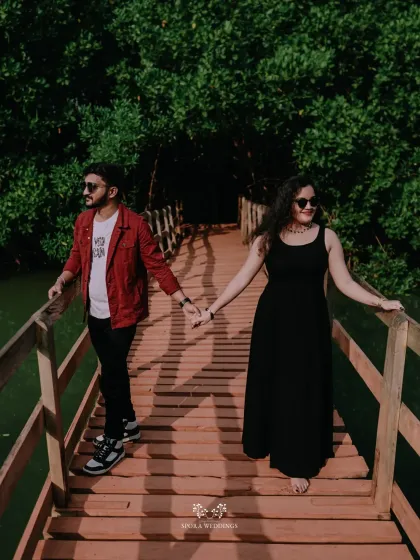The couple holding hands on a wooden bridge, the strong lines of the bridge contrasting with the natural surroundings.