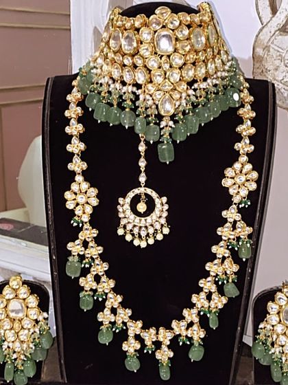 This grand Kundan set features a choker and a floral-motif long necklace with light green beads. It's a complete rental set with matching oversized earrings and a maang tikka.