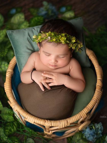 This little prince is sleeping in his basket throne, surrounded by greenery. The earthy tones of the wrap and the fresh floral crown create a natural, organic feel.