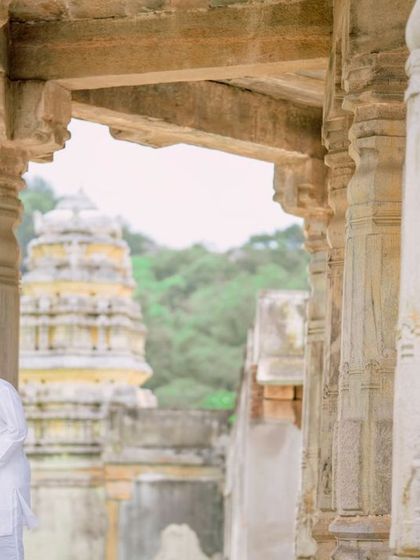 An intimate moment shared between a couple dressed in traditional attire, using the texture and history of a temple pillar as a backdrop for their love story.